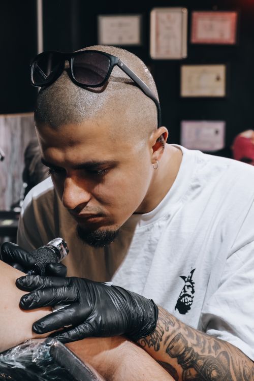 Free Tattoo artist intensely focused on creating a detailed design inside a studio setting. Stock Photo