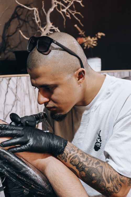 Free A skilled tattoo artist intensely focuses on creating a detailed arm design indoors. Stock Photo