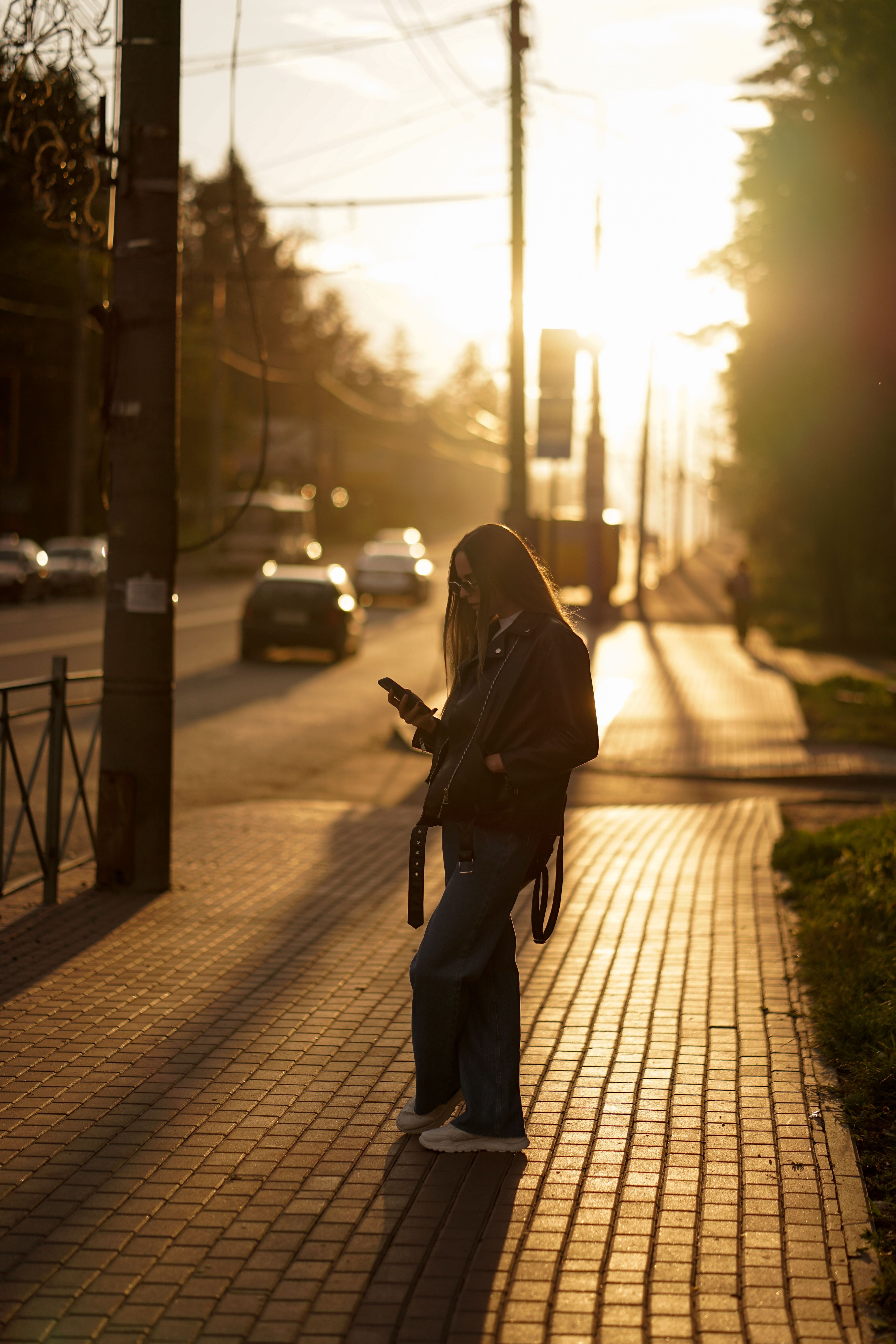 Person checking a phone on a sunlit street at dusk, photo by Solomiia Voloshyn on Pexels