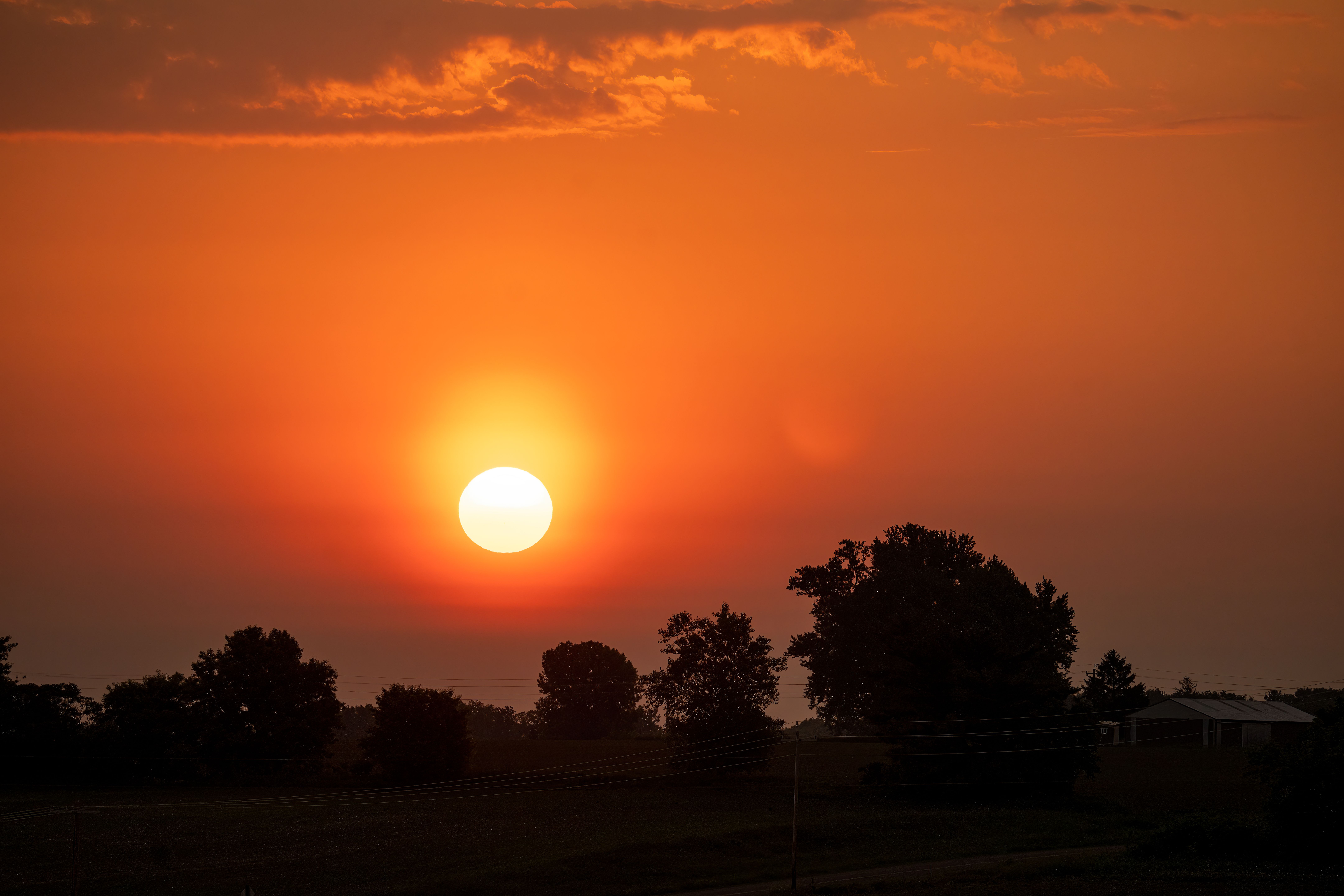 Captivating sunset over rural landscape in Lund, WI, silhouetting trees and fields.