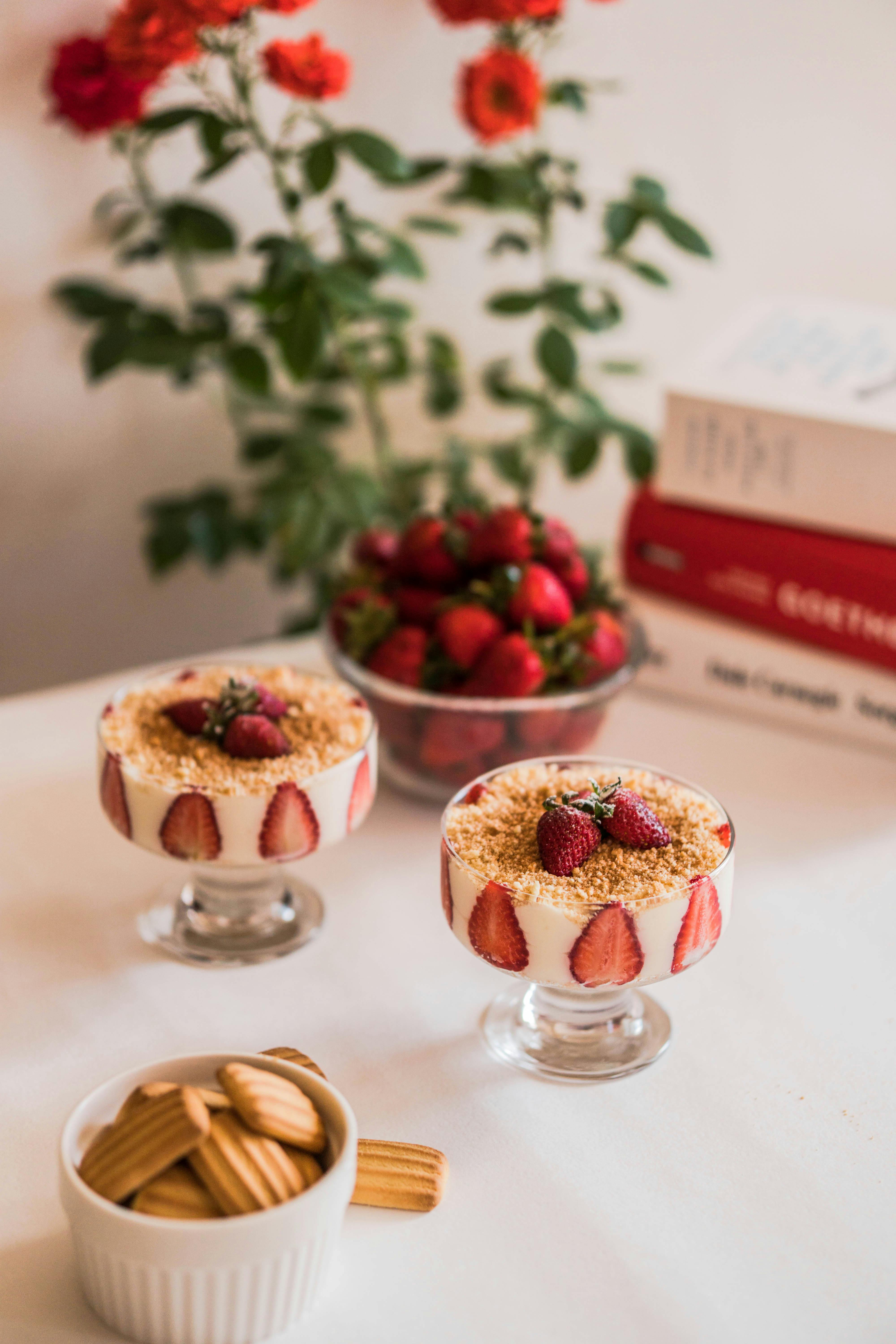 Elegant strawberry desserts with cream, biscuits, and fresh fruit on a table.
