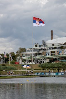 Serbian flag flies high over Belgrade's waterfront with cityscape and park view.