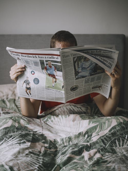 Free Man Lying in Bed Reading Newspaper Stock Photo