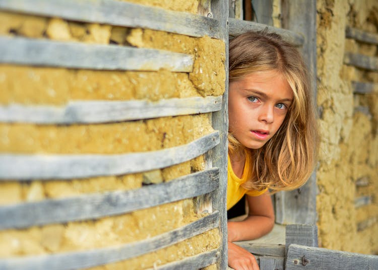 Blonde Girl Looking Out Window Of Rural House