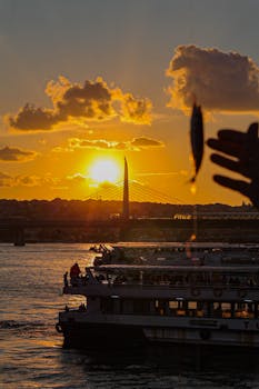 Silhouetted Bosphorus bridge and ferries at sunset in Istanbul, vibrant sky with fishing silhouette.