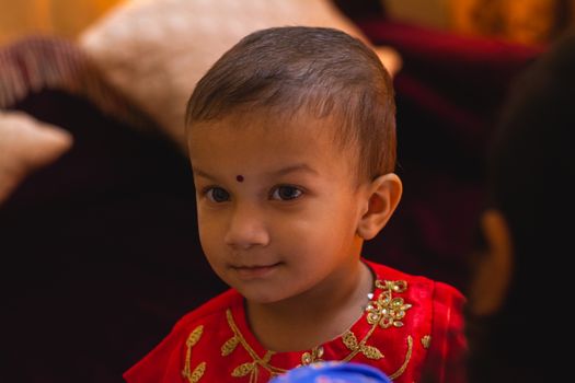 Adorable child wearing traditional Indian clothing, smiling gently indoors.