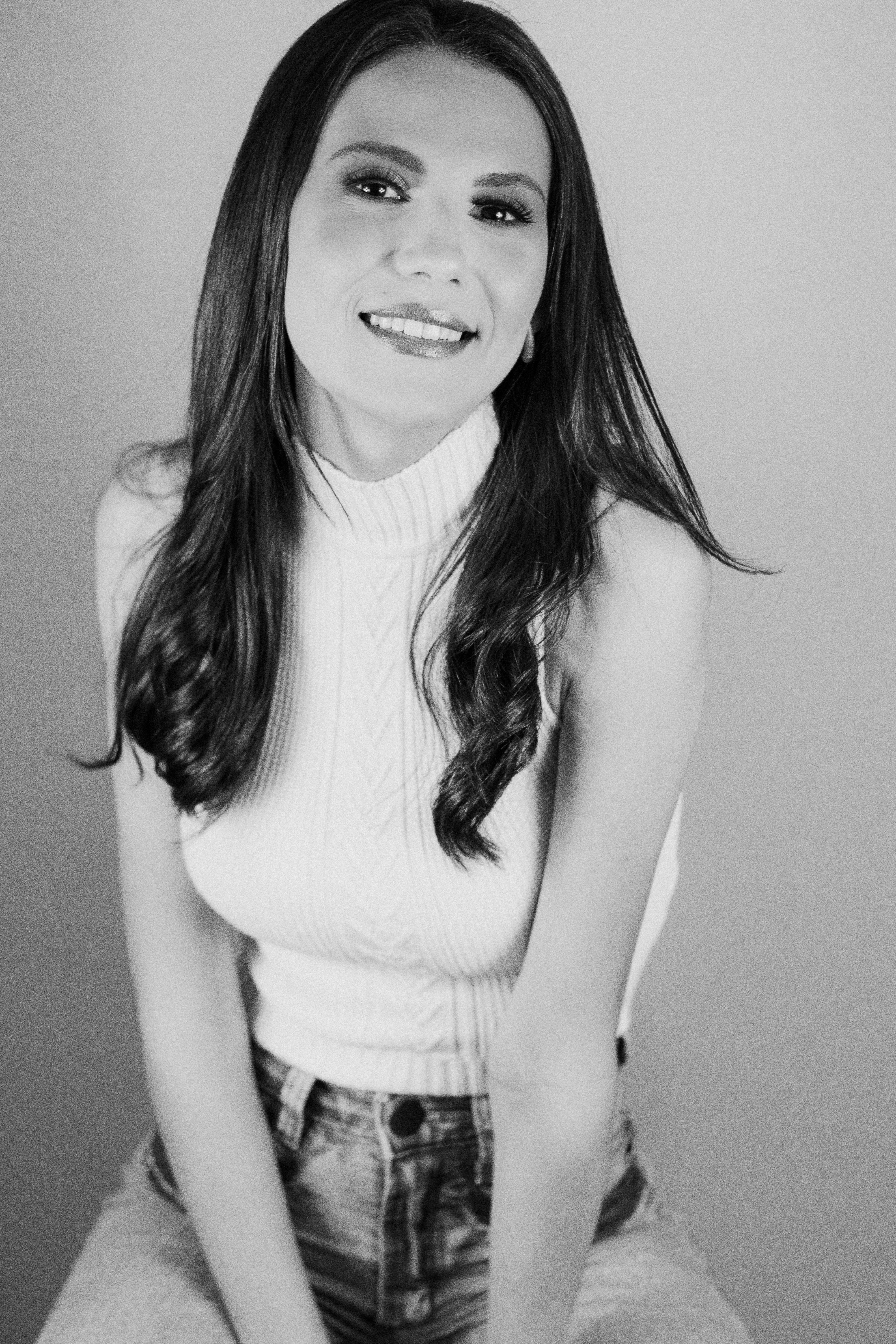 Elegant black and white portrait of a woman smiling in a studio setting, wearing a sleeveless turtleneck.