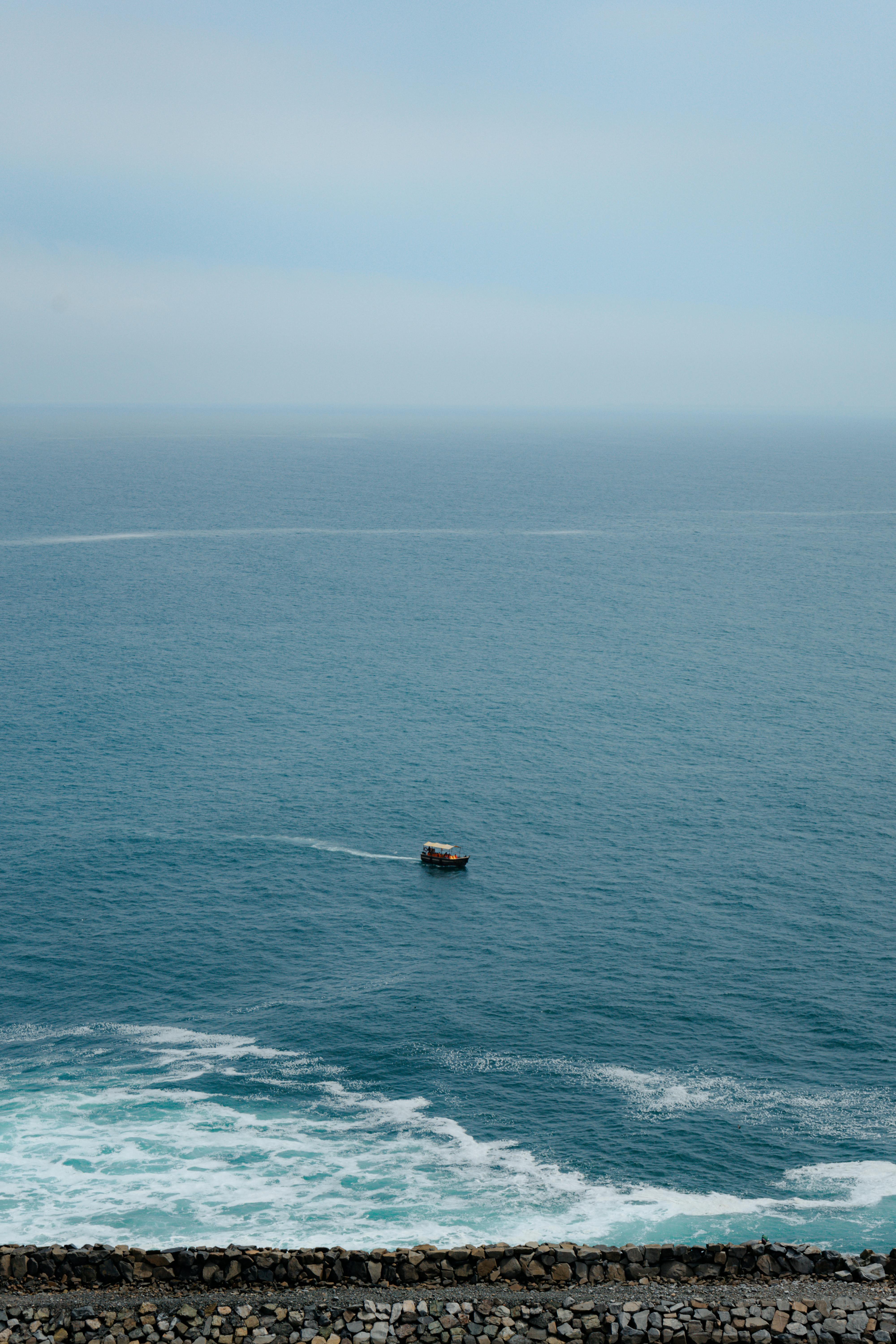 A tranquil high-angle view of a lone motorboat on the vast blue ocean near a rocky shore, showcasing peaceful seascape beauty.