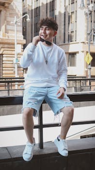 Young man in stylish attire sitting by urban railing, embodying city fashion.