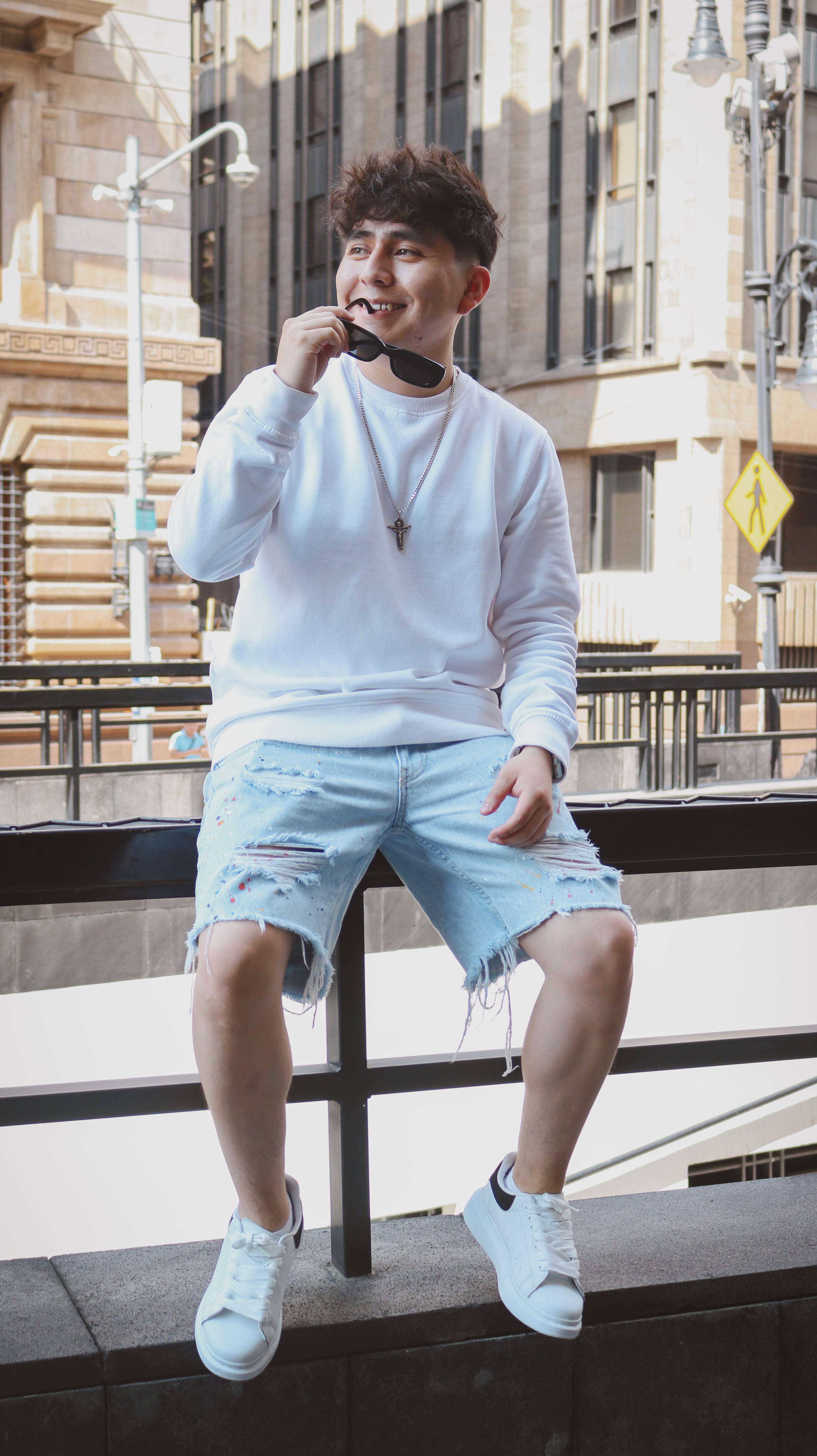 Jovem homem em traje estiloso sentado perto de um corrimão urbano, incorporando a moda da cidade.