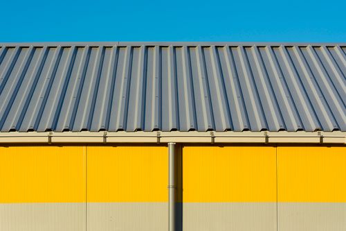 Free Photo of a yellow warehouse wall with a corrugated metal roof under a clear blue sky. Stock Photo