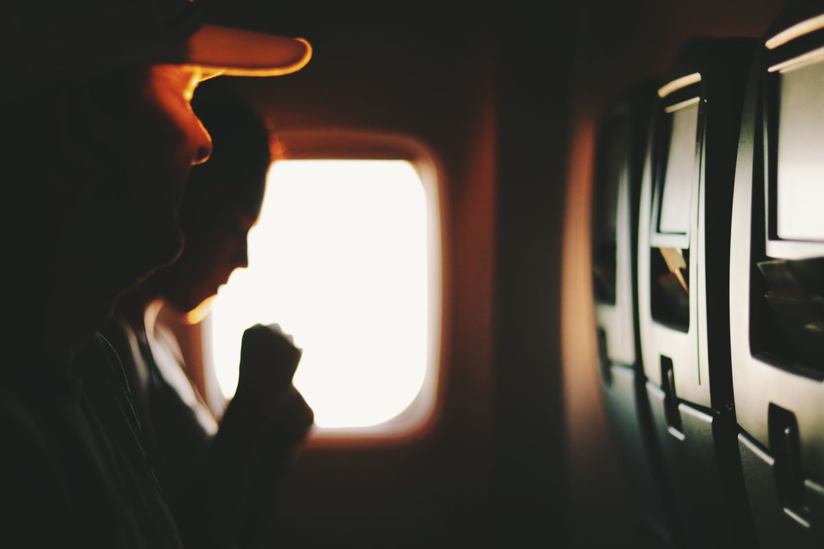 Silueta unui pasager la fereastra avionului, in contralumina calda