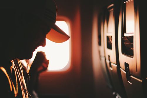 Free A silhouette of a traveler enjoying a quiet moment on an airplane, illuminated by sunrise through the window. Stock Photo