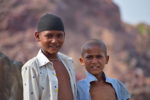 Two boys smiling outdoors against a natural rocky background.