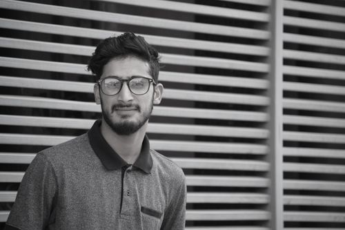 Free Stylish monochrome portrait of a young man wearing glasses posing against a modern wall background. Stock Photo