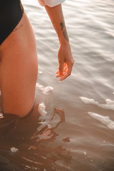 Close-up of a tattooed woman standing in water at sunset, capturing serenity and natural beauty.