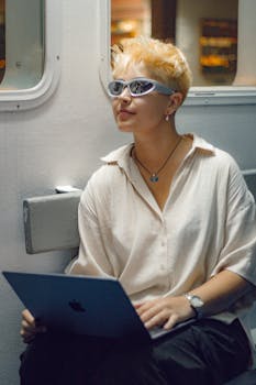 Trendy young woman with sunglasses using a laptop in a modern indoor space.