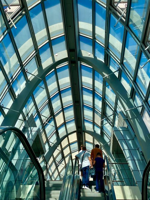 Free Two adults on an escalator in a modern atrium with a glass ceiling and structural beams, daytime. Stock Photo
