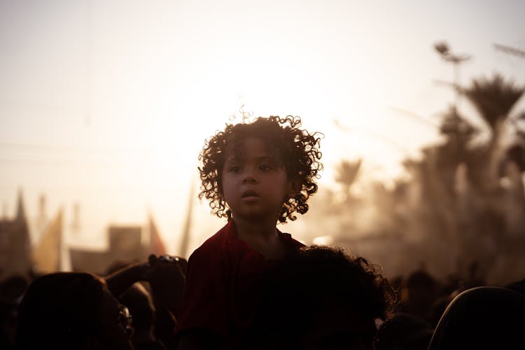 A Child Sitting On A Persons Shoulders In The Crowd At A Parade 