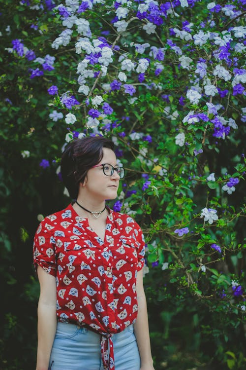 Woman Wearing Red and Blue Shirt Standing Beside Purple and White Flowers