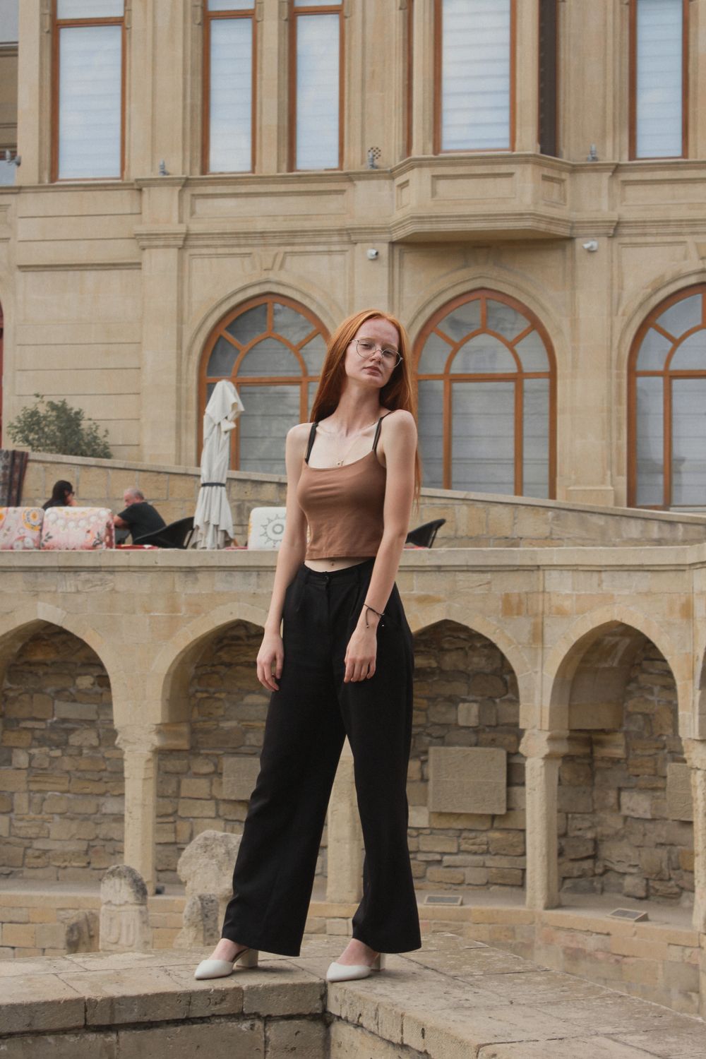 Schwarze weite Hose mit braunem Top und hellen Schuhen vor einer Fassade