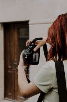 A redhead woman photographing with a digital camera outside a building.