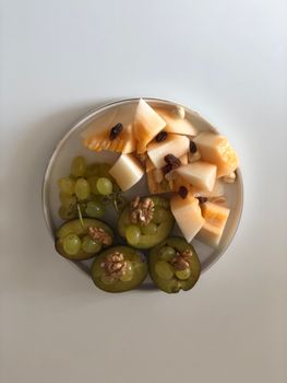 A delicious assortment of grapes, melons, and walnuts on a white plate, photographed from above.