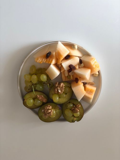 Free A delicious assortment of grapes, melons, and walnuts on a white plate, photographed from above. Stock Photo