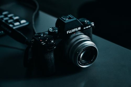 Free Detailed image of a Fujifilm mirrorless camera on a dark table, showcasing lens and design. Stock Photo