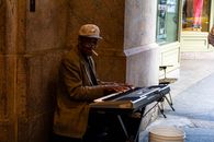 Street musician playing keyboard outside a building in an urban setting, smoking a cigarette.