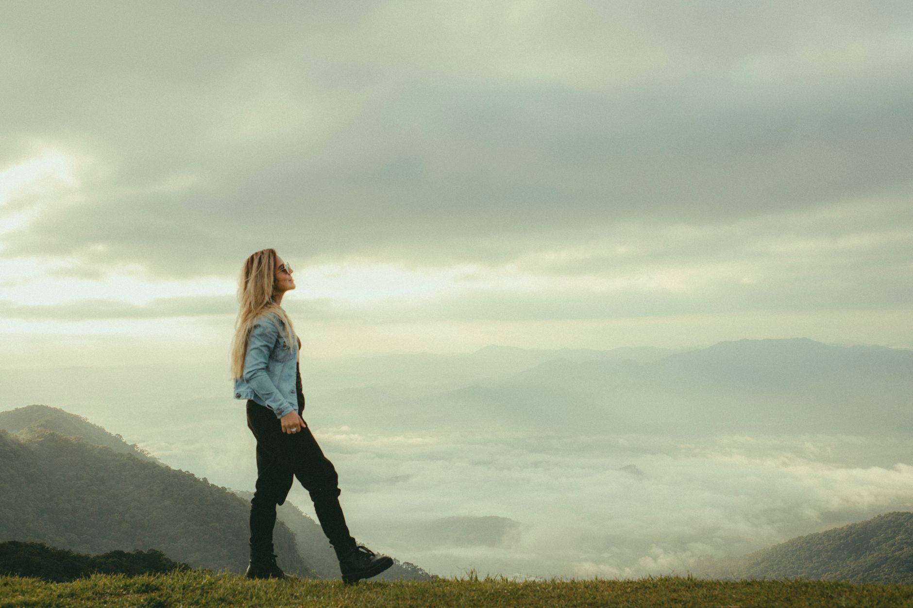 A woman in a denim jacket walks along a misty mountain landscape, enjoying a scenic view.