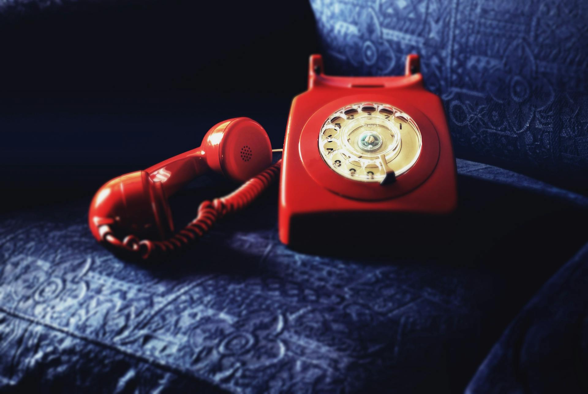 A classic red rotary phone placed on an elegant blue textured fabric, evoking nostalgia.