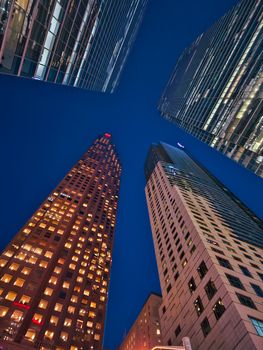 Dramatic upward view of illuminated skyscrapers at night in a bustling city downtown.