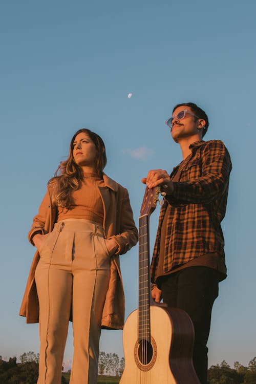 Woman in Brown Coat and Man with a Guitar Posing at Sunset