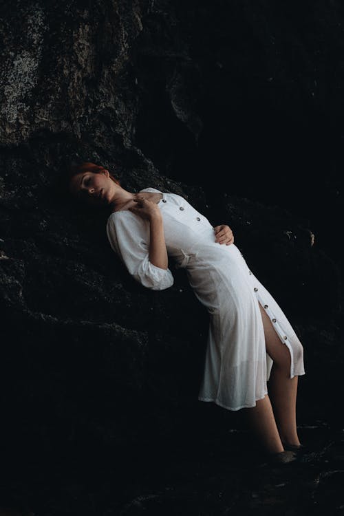 Woman in White Clothes Leaning on Rocks and Posing