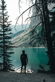A man stands by a turquoise lake in Banff, Canada, with mountains in the backdrop.