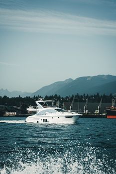 A luxury yacht cruising in Vancouver Harbor with mountains in the background, captured on a clear day.