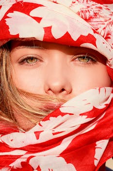 Close-up photo of a woman with green eyes and red floral scarf covering her head, evoking mystery.