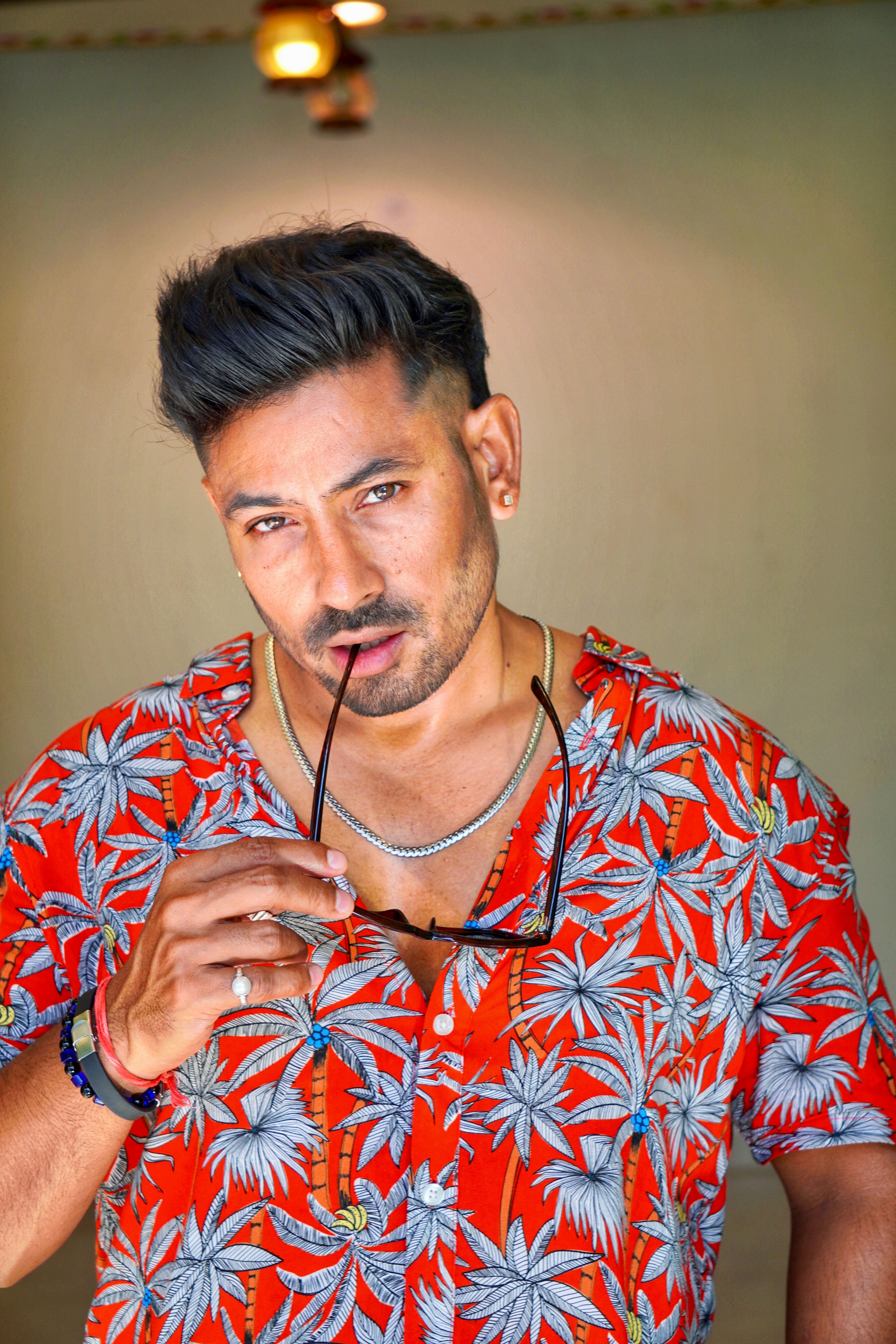 Confident man in tropical shirt posing with sunglasses indoors.