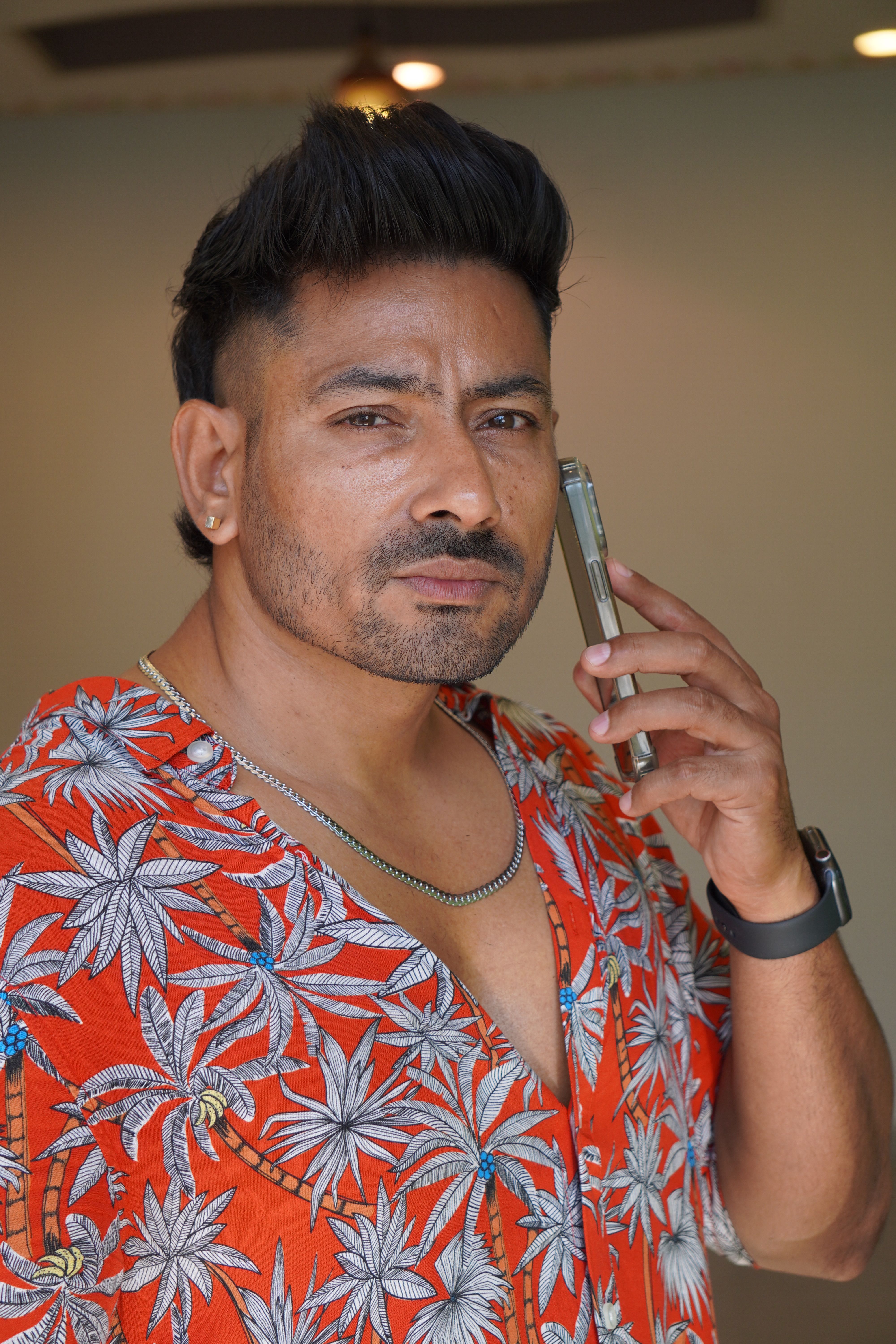 Confident man in red floral shirt using smartphone, highlighting modern lifestyle.