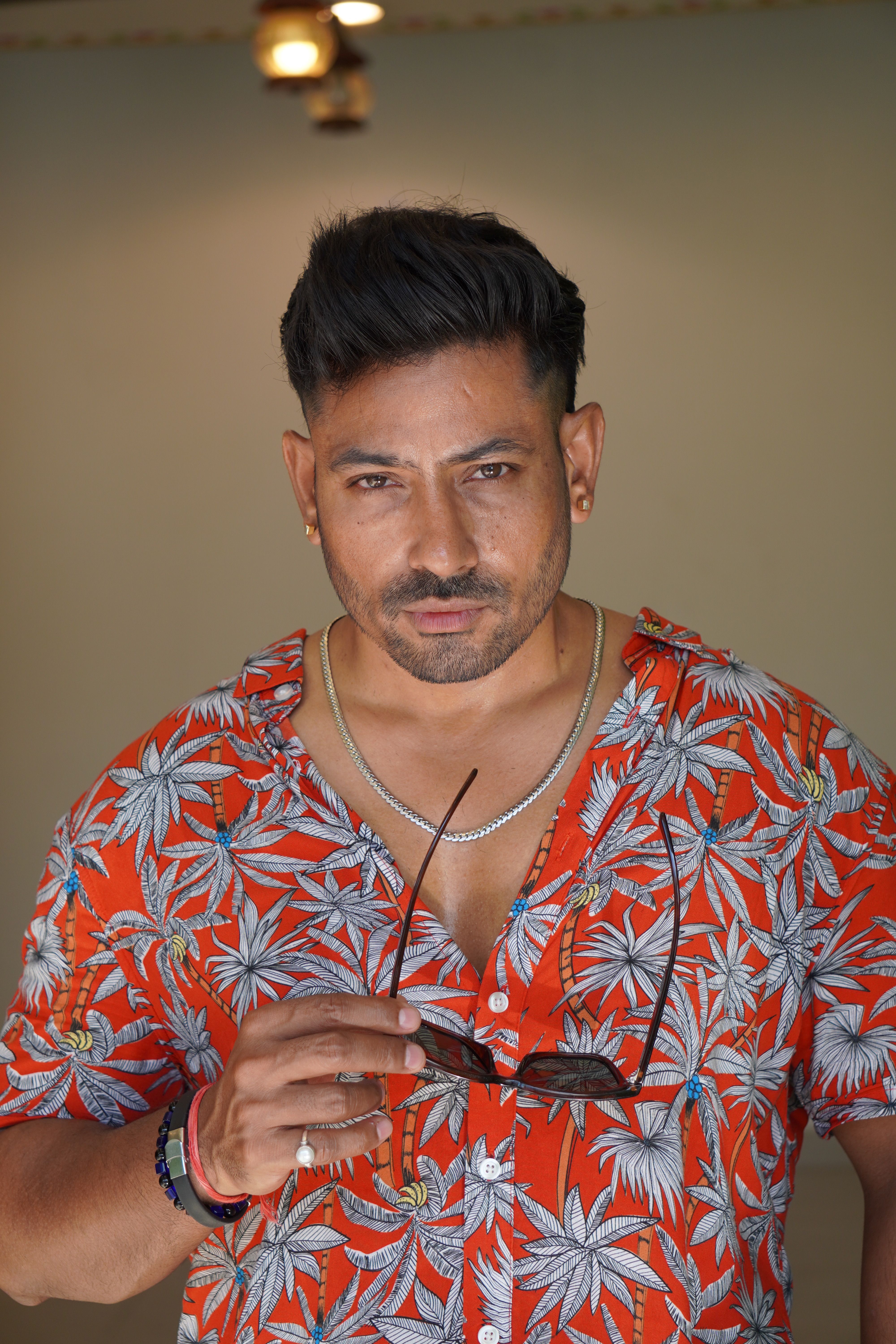 Confident man in a tropical shirt holding sunglasses, exuding style and charm.