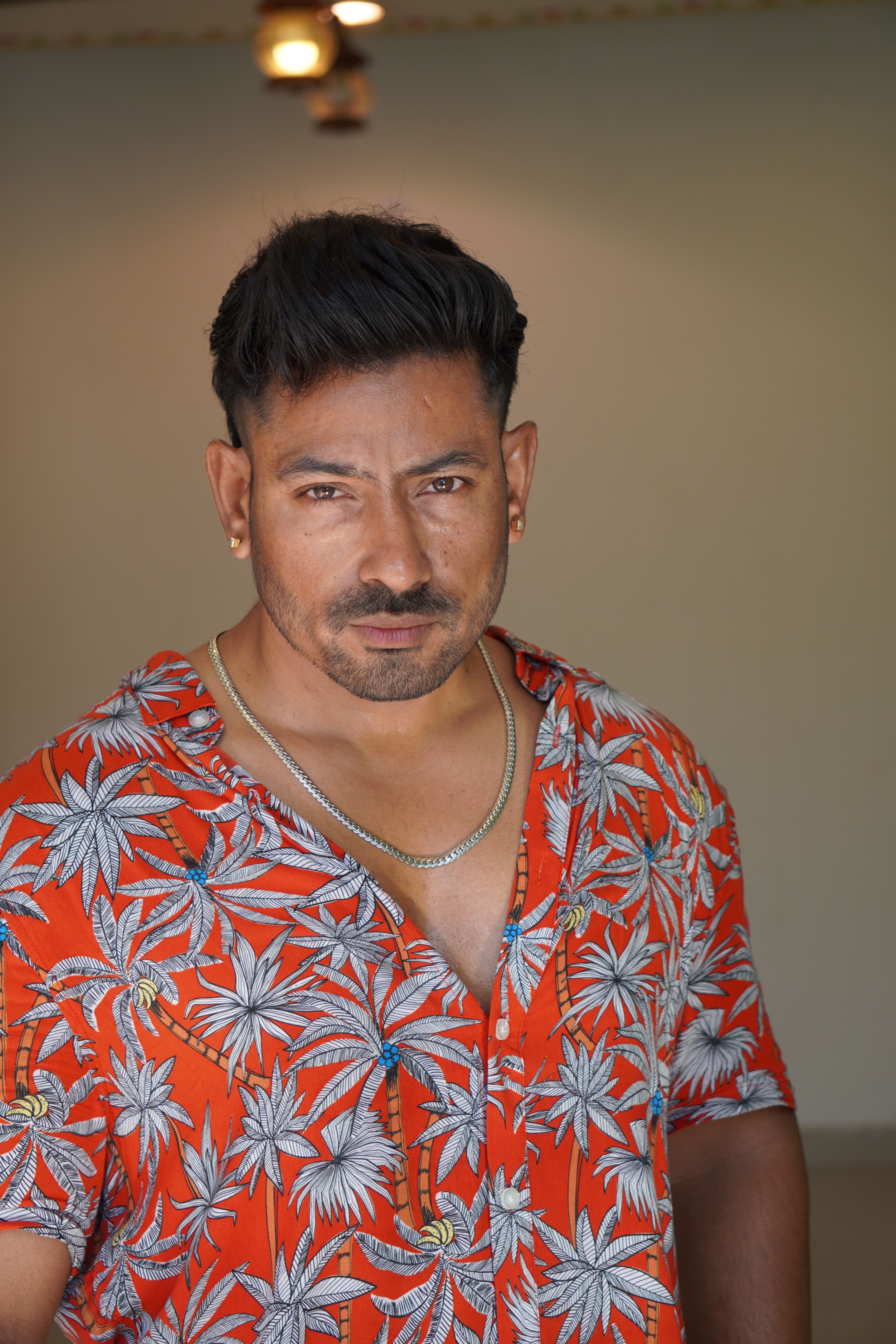 A muscular man in a vibrant tropical shirt poses confidently indoors.