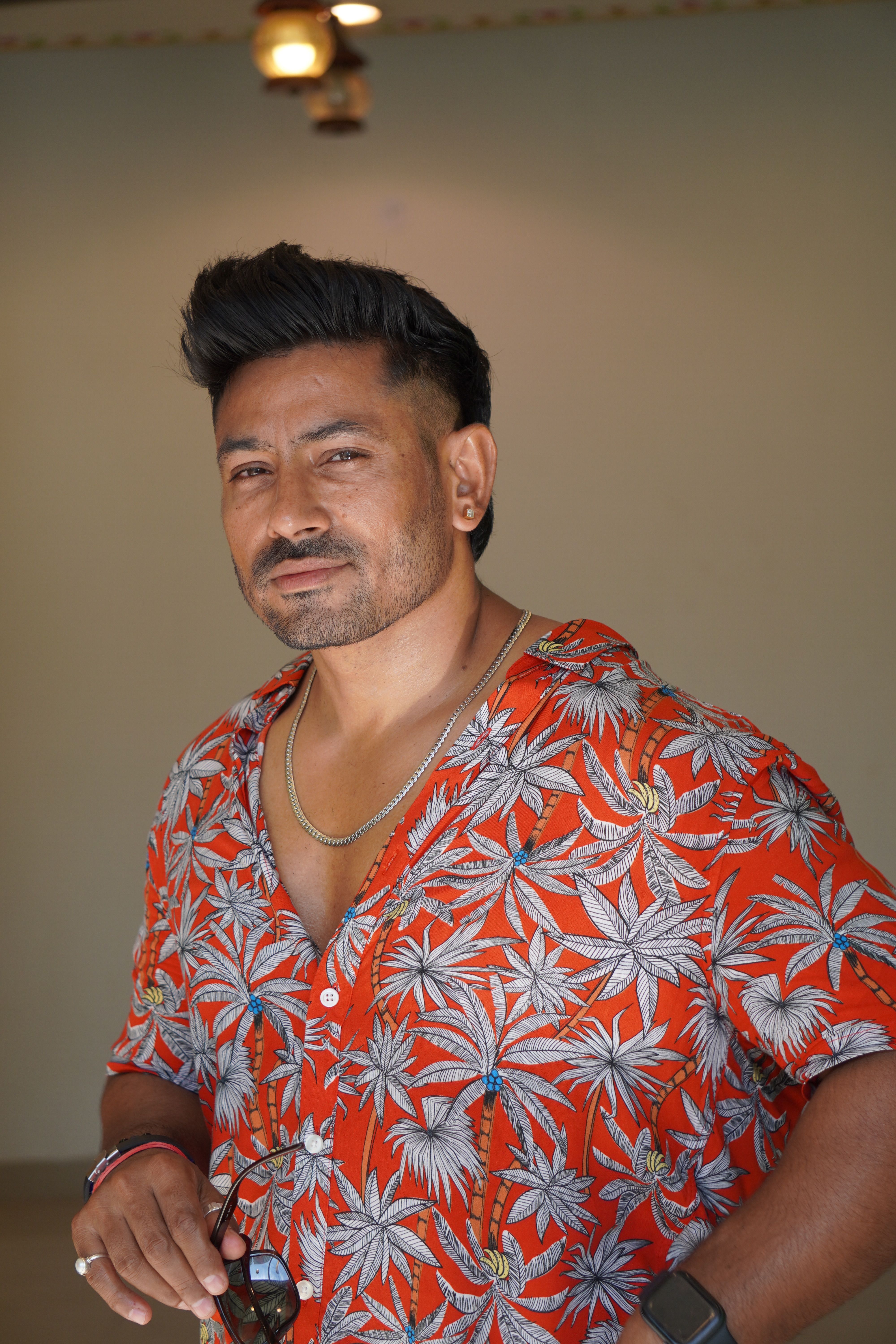 A confident man in a vibrant tropical shirt poses indoors, exuding charisma and style.