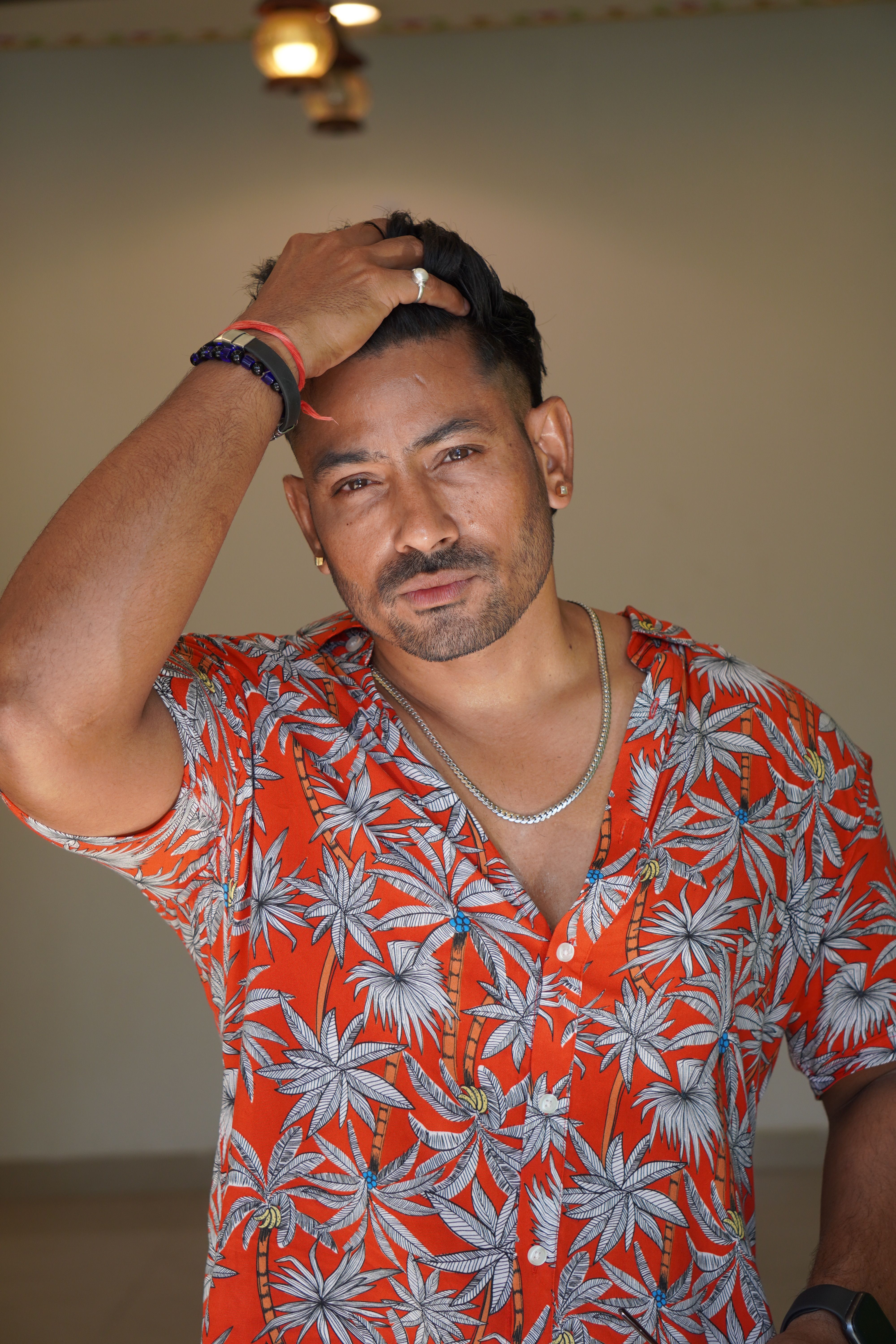 A man in a vibrant tropical shirt poses confidently indoors, showcasing fashion and style.