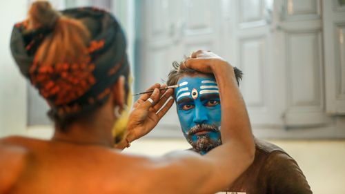 Free A man gets vibrant face paint applied in a traditional Indian cultural setting. Stock Photo