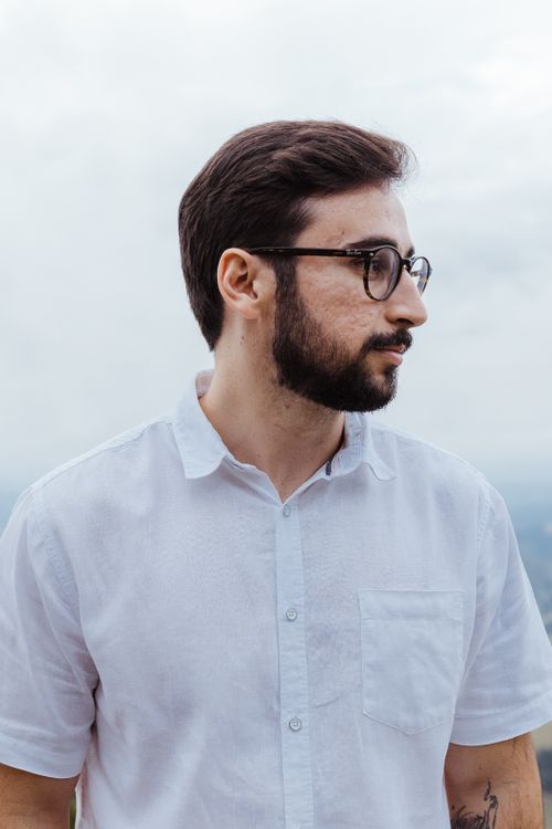 Free Serious man in eyeglasses and shirt with tattoos, standing outdoors. Stock Photo