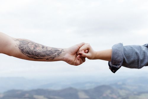 Free Close-up of two arms interlocking with a tattooed arm against a scenic backdrop. Stock Photo