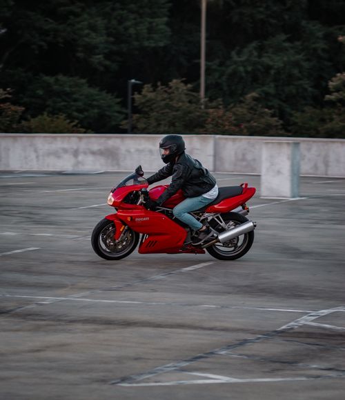 Free A motorcyclist on a red bike riding through an empty parking lot. Urban adventure captured. Stock Photo