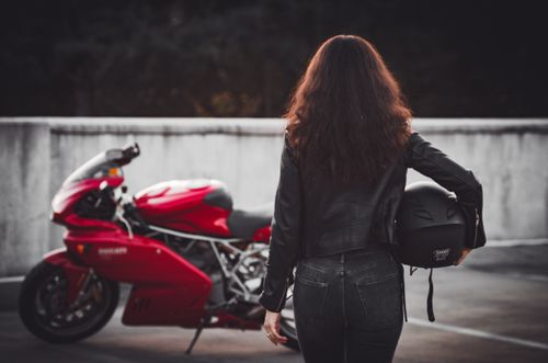 Free Back view of a woman with a helmet near a stylish red motorcycle on an outdoor lot. Stock Photo