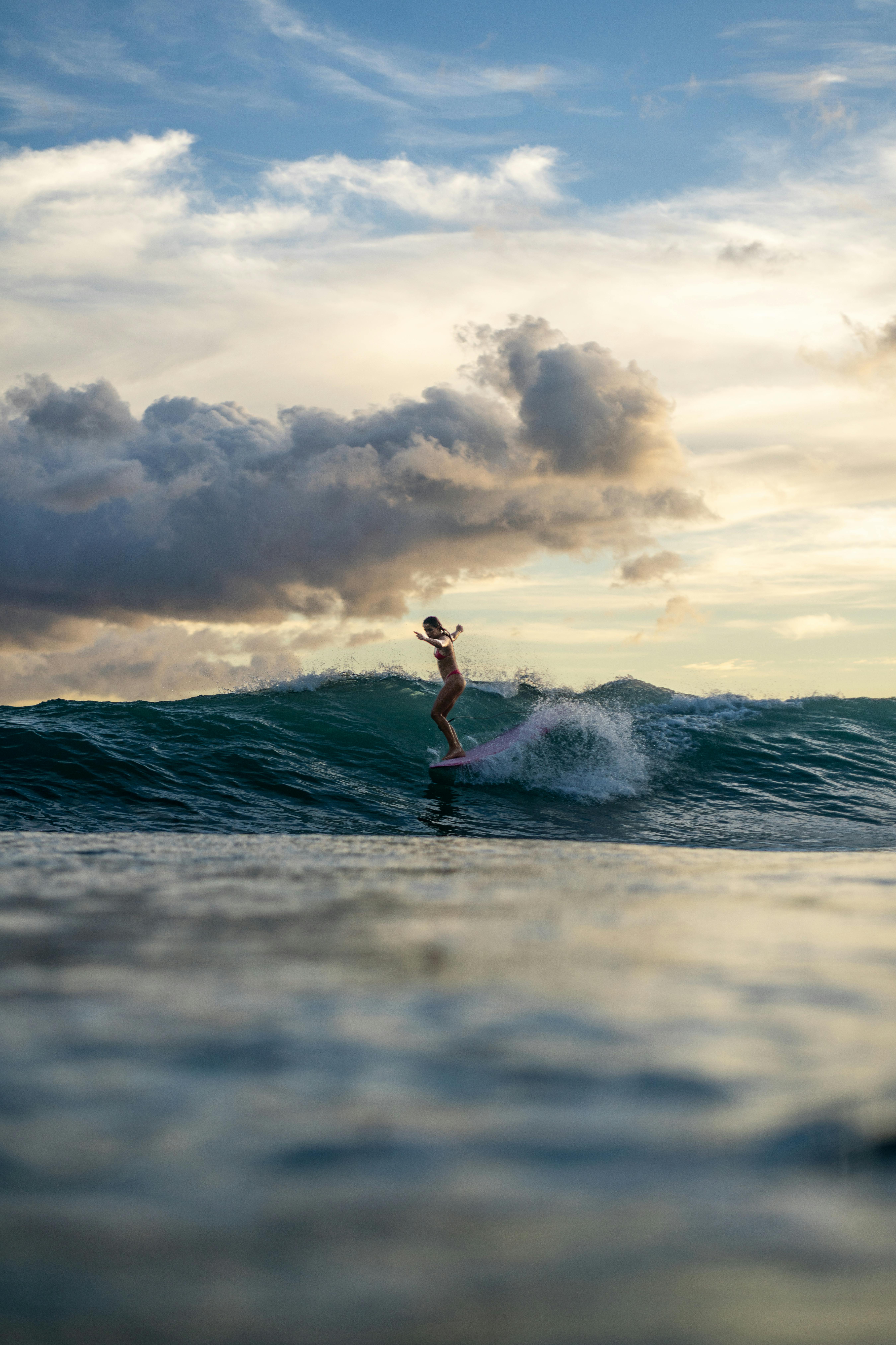 A woman surfs on a wave against a vibrant sunset in Honolulu, Hawaii.